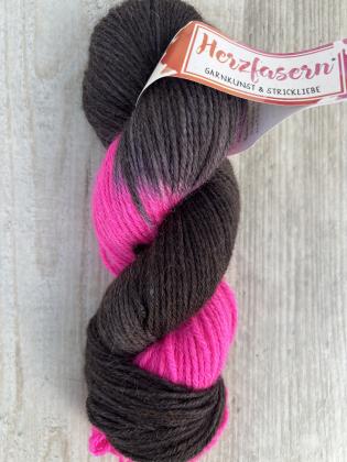 Handgefärbter Wollstrang Herzfasern No. 46 aus Alpaka und Bio-Schurwolle in dunklem Schokoladenbraun mit leuchtenden Neonpink-Akzenten, fotografiert auf hellem Holzuntergrund.